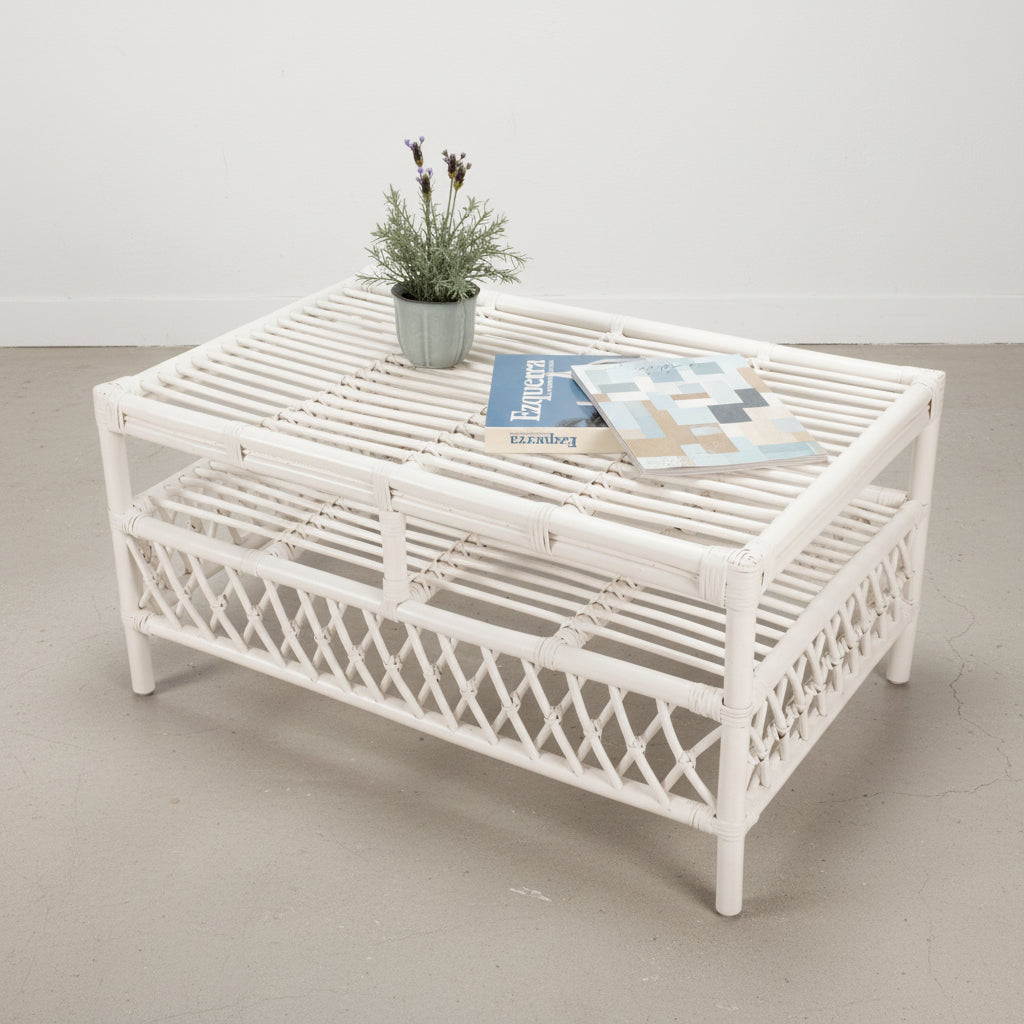A white rattan coffee table with a cross motif design, featuring a plant and a magazine on its surface.